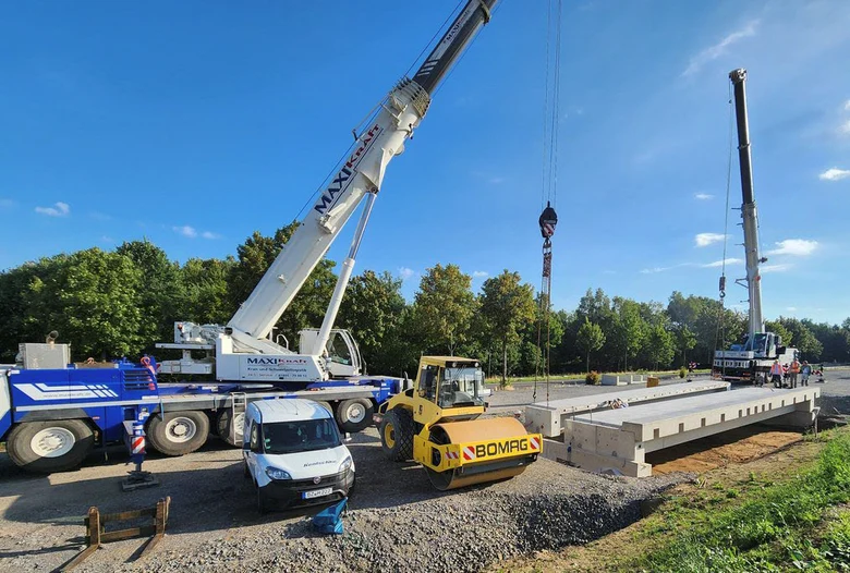 Baustellensituation im Tiefbau mit zwei Kränen, einer Planierraupe und einigen großen Betonferteilen
